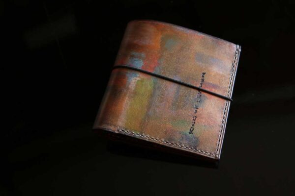 手染めによる抽象アート柄が美しい一点物の本革レザーノートカバー。ブラウンをベースに青・緑・赤・黄が重なり、ゴムバンドで留めるシンプルなデザイン。
