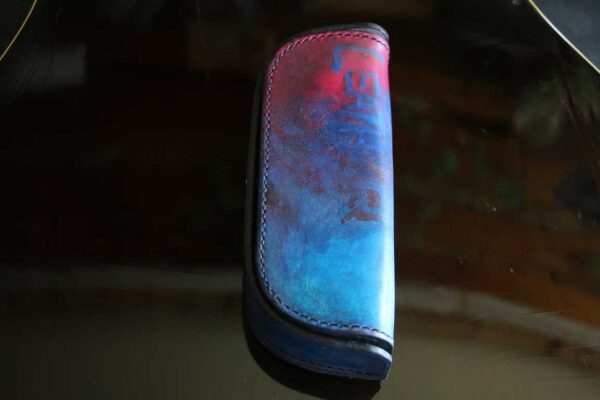 一点物のThe Crescent Moon Glasses case。ターコイズブルーからネイビーへと移ろうグラデーションに、深紅のアクセントを重ねた本革メガネケース。内装には起毛革を使用した三日月型デザイン。