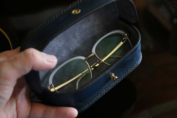 一点物のThe Crescent Moon Glasses case。ターコイズブルーからネイビーへと移ろうグラデーションに、深紅のアクセントを重ねた本革メガネケース。内装には起毛革を使用した三日月型デザイン。