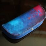一点物のThe Crescent Moon Glasses case。ターコイズブルーからネイビーへと移ろうグラデーションに、深紅のアクセントを重ねた本革メガネケース。内装には起毛革を使用した三日月型デザイン。