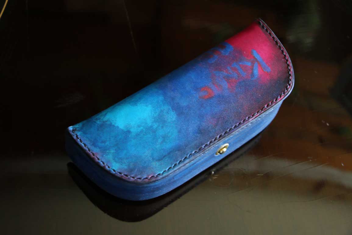 一点物のThe Crescent Moon Glasses case。ターコイズブルーからネイビーへと移ろうグラデーションに、深紅のアクセントを重ねた本革メガネケース。内装には起毛革を使用した三日月型デザイン。